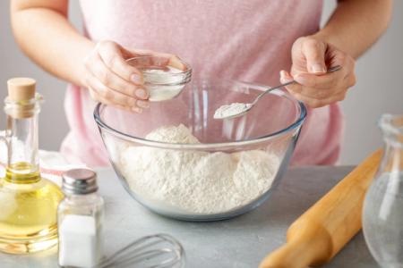 A woman is mixing baking powder in a glass bowl with a spoon.