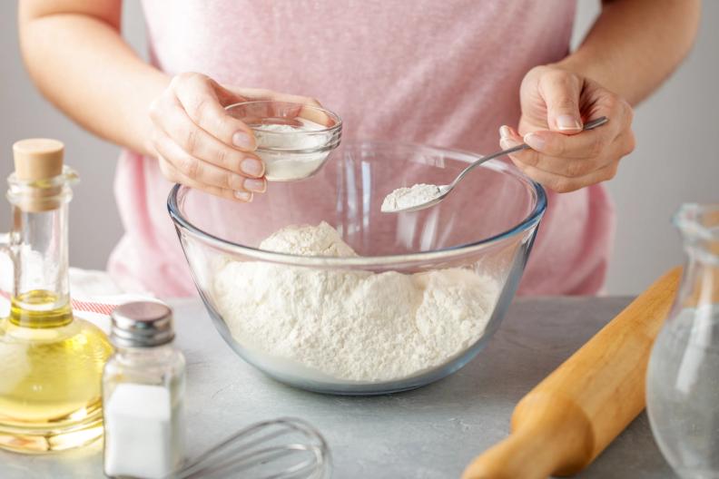 A woman is mixing baking powder in a glass bowl with a spoon.