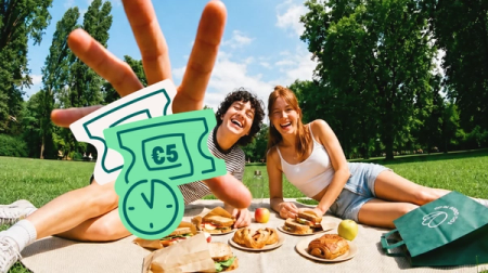 Two people happily picnicking in a park with food and a "Too Good To Go" bag, overlaid with a peace sign, €5 discount tickets, and a clock icon.
