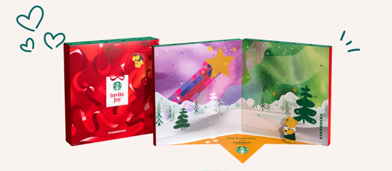 Open Starbucks 'Invite Joy' advent calendar revealing festive snowy scenes and a small yellow bear plush.