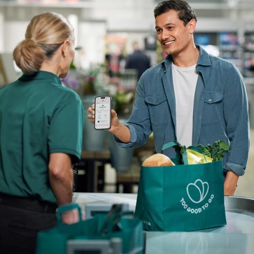a man is holding a cell phone in front of a bag that says too good to go