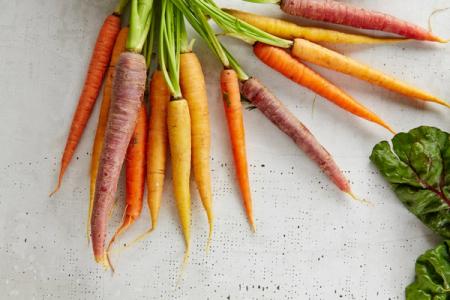 a bunch of carrots of different colors are sitting on a table .