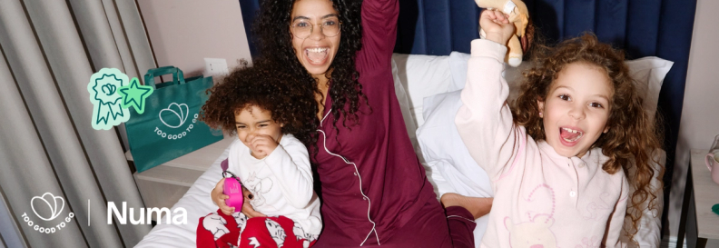 A joyful woman and two children in pajamas celebrate together on a bed, with "Too Good To Go" branding and "Numa" text.