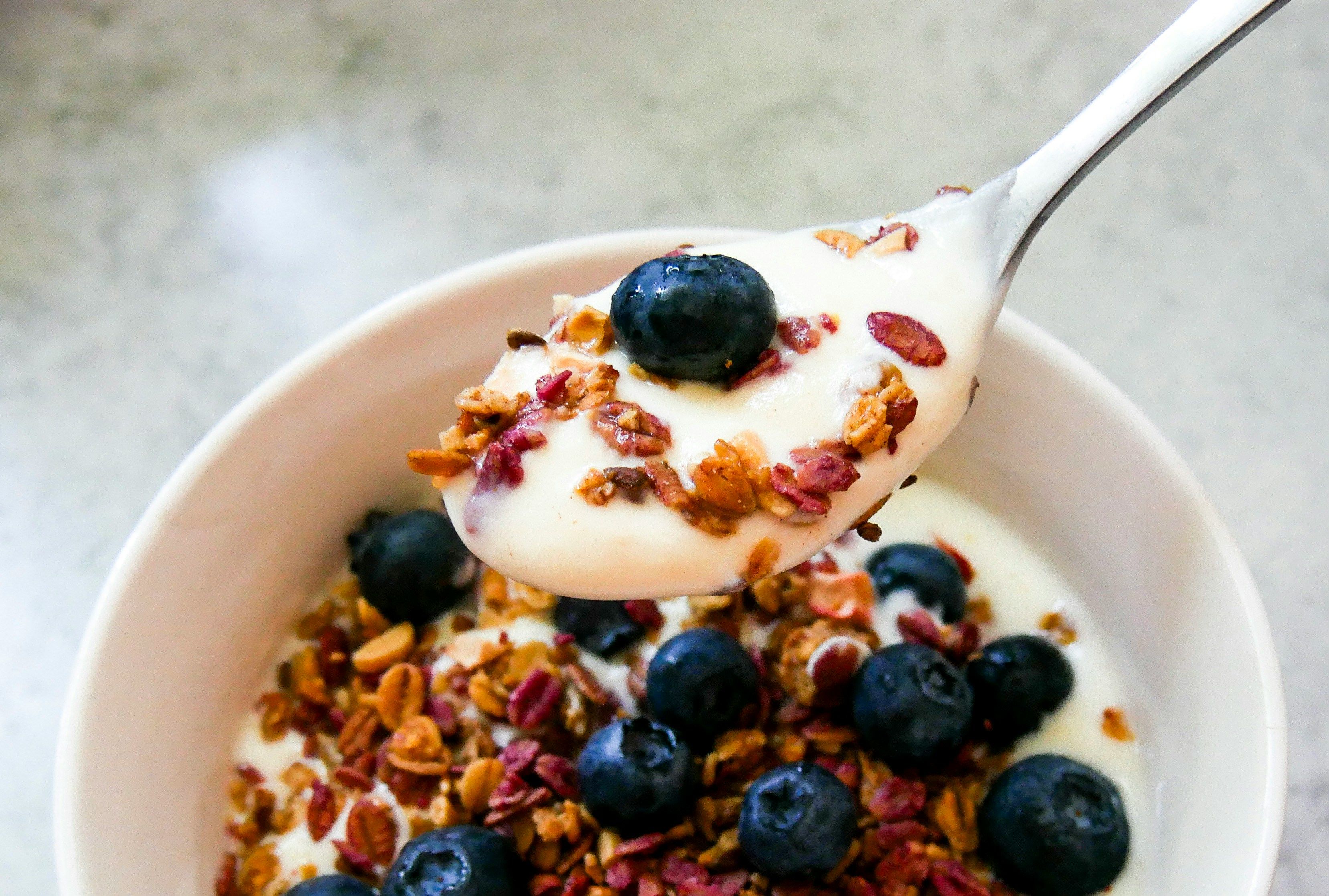 a spoon is holding a spoonful of yogurt over a bowl of granola and blueberries .