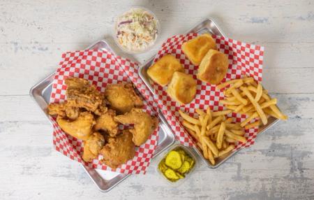 two trays of fried chicken , french fries , biscuits and coleslaw on a wooden table .