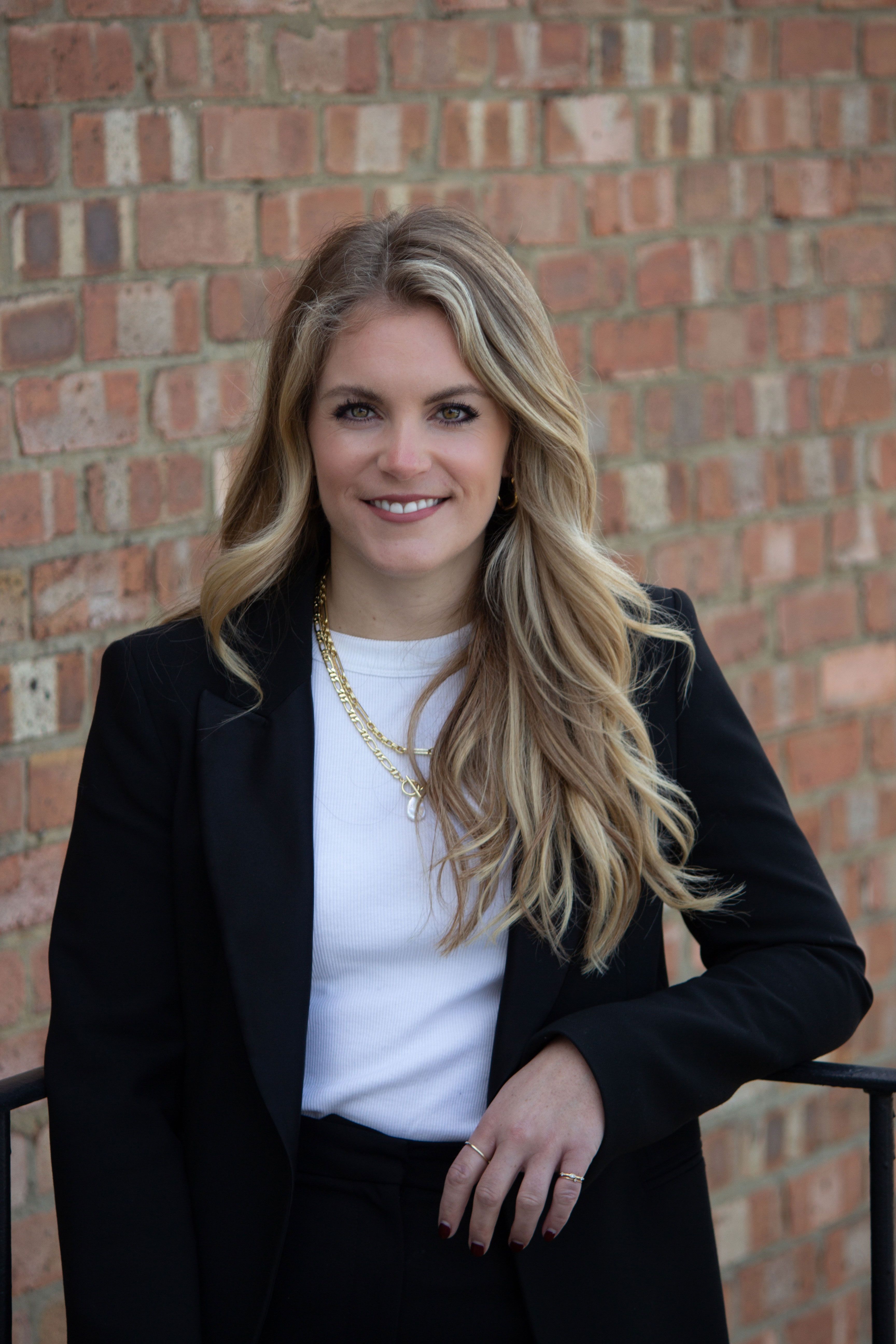 a woman wearing a black jacket and a white shirt is standing in front of a brick wall