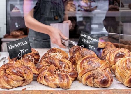 Swedish cinnamon and cardamom buns on display in a bakery, with a person behind the counter.
