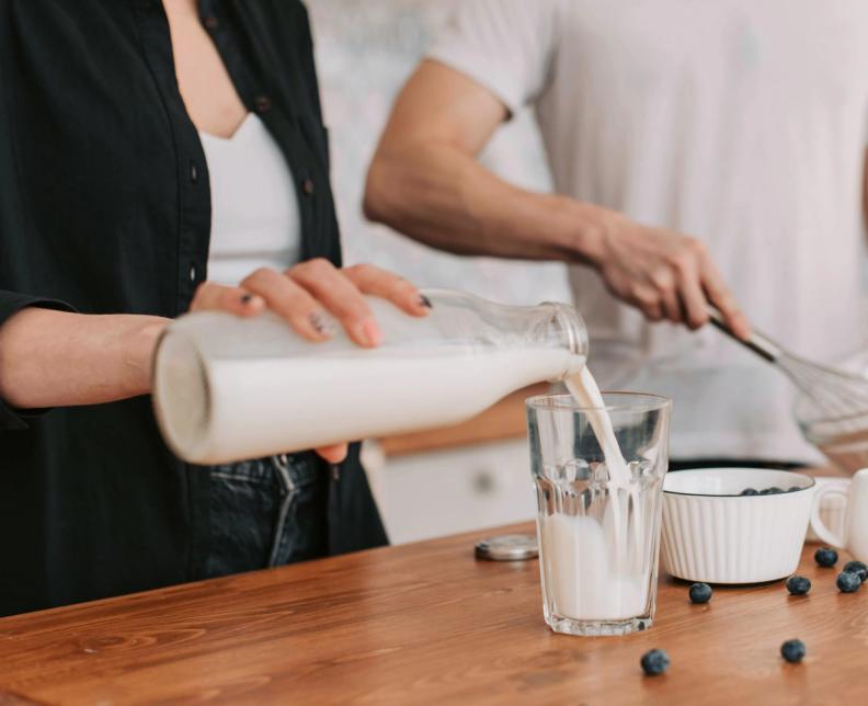 a woman is pouring milk into a glass on a wooden counter .