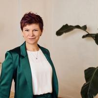 a woman in a green suit and white shirt is standing in front of a plant .