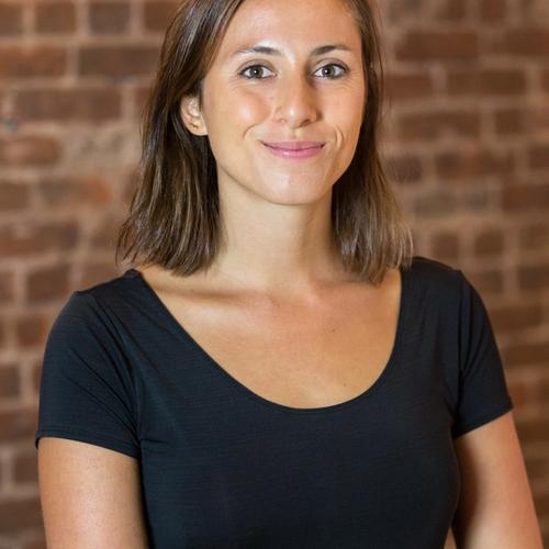 a woman in a black shirt stands in front of a brick wall
