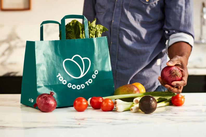 a man is holding an apple in front of a bag of vegetables .