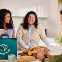 a man and two women are sitting at a table with a bag of food .