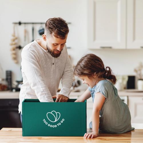 a man and a little girl are sitting at a table looking at a box .