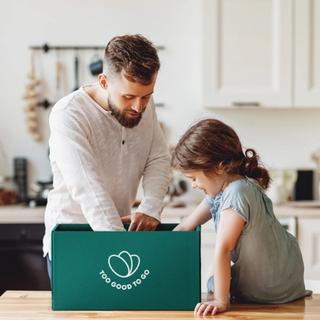a man and a little girl are sitting at a table looking at a box .