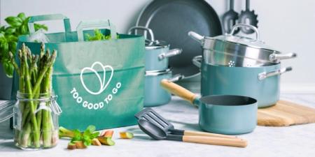a kitchen counter with pots and pans , asparagus , and a bag of food .