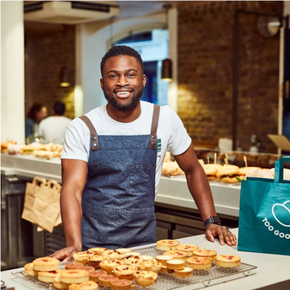 a man in an apron stands in front of a table full of pastries