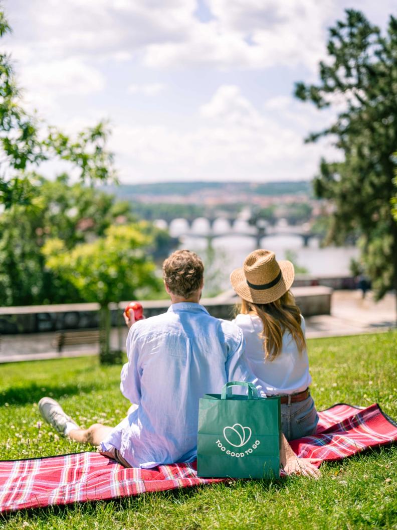 a man and woman sitting on a blanket with a bag that says too good to go