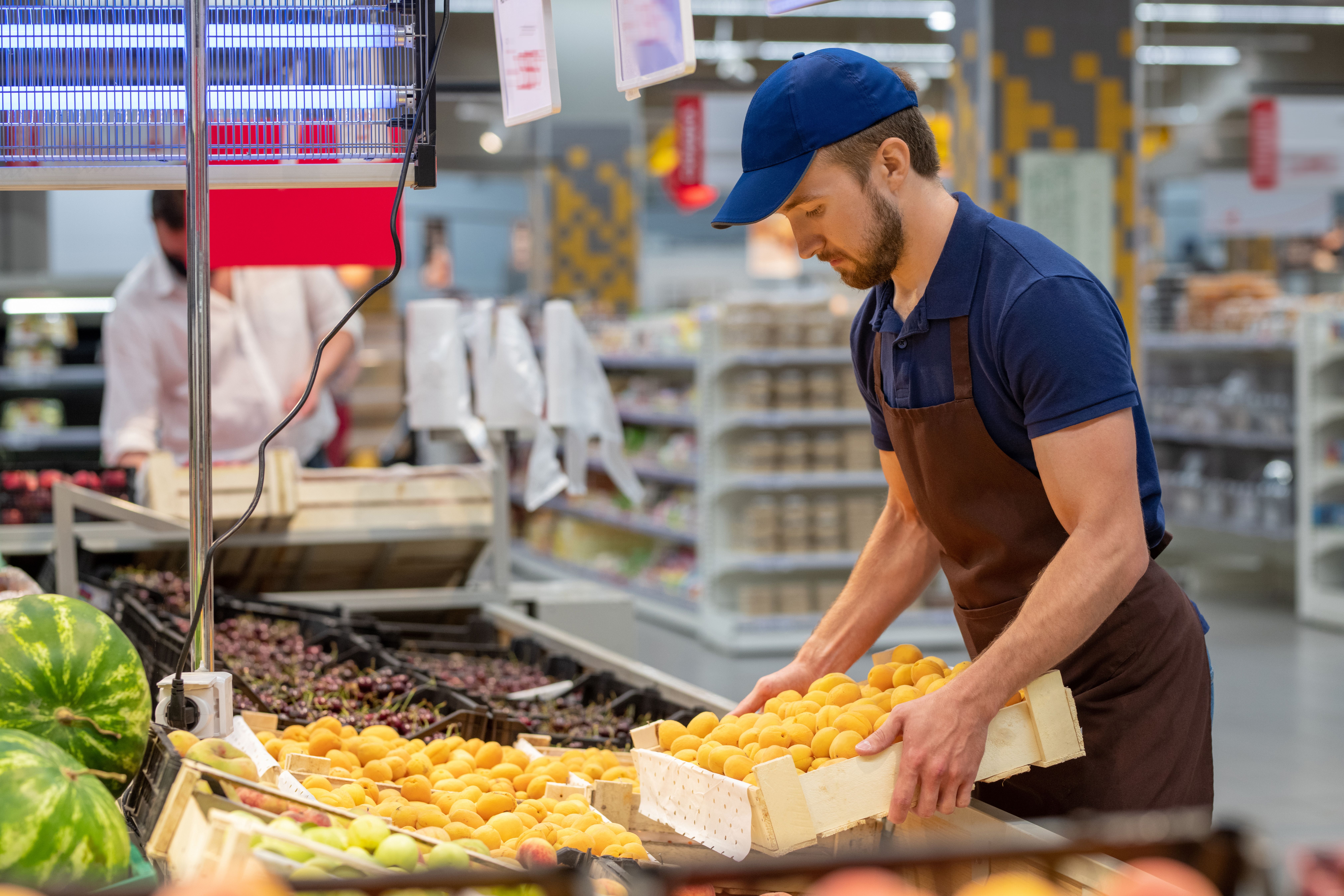A man in an apron and cap stocking potatoes in a supermarket.