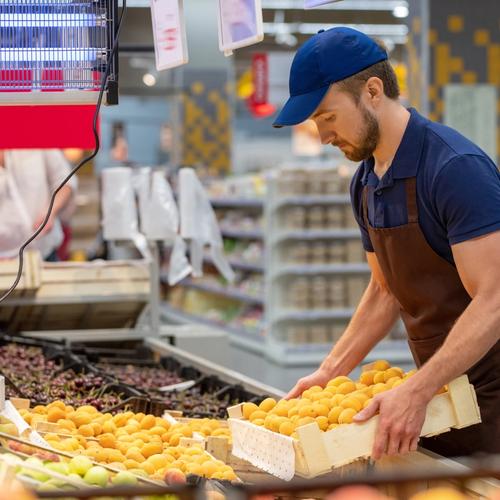A man in an apron and cap stocking potatoes in a supermarket.
