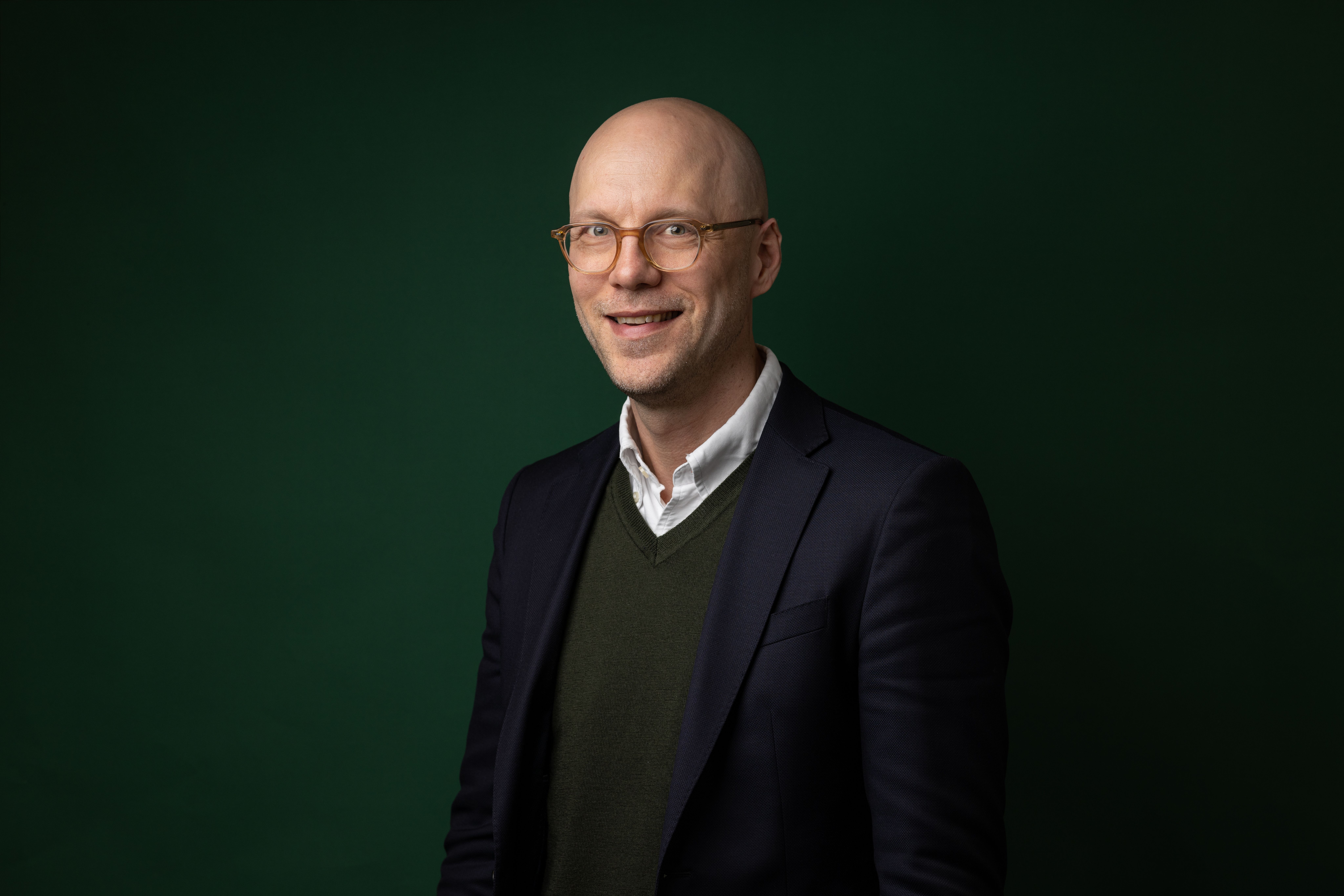 a bald man wearing glasses and a suit is smiling in front of a green background .