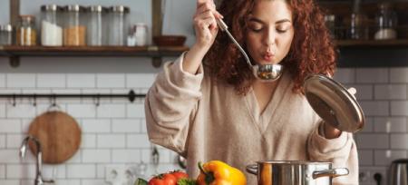 Woman with curly red hair cooling food in a ladle in a kitchen.