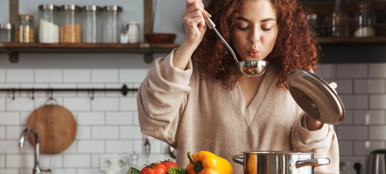 Woman with curly red hair cooling food in a ladle in a kitchen.