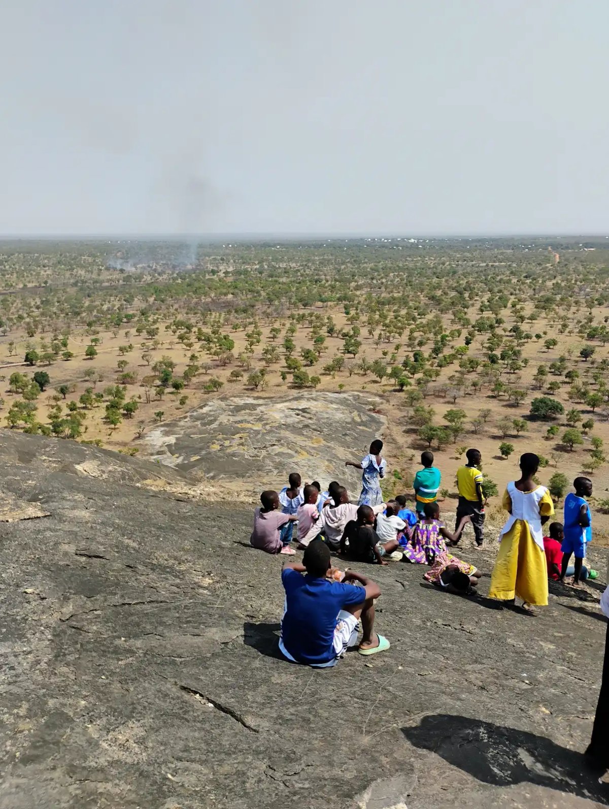 Children and adults sitting on the summit of Uombo Rock overlooking the Upper West Region landscape