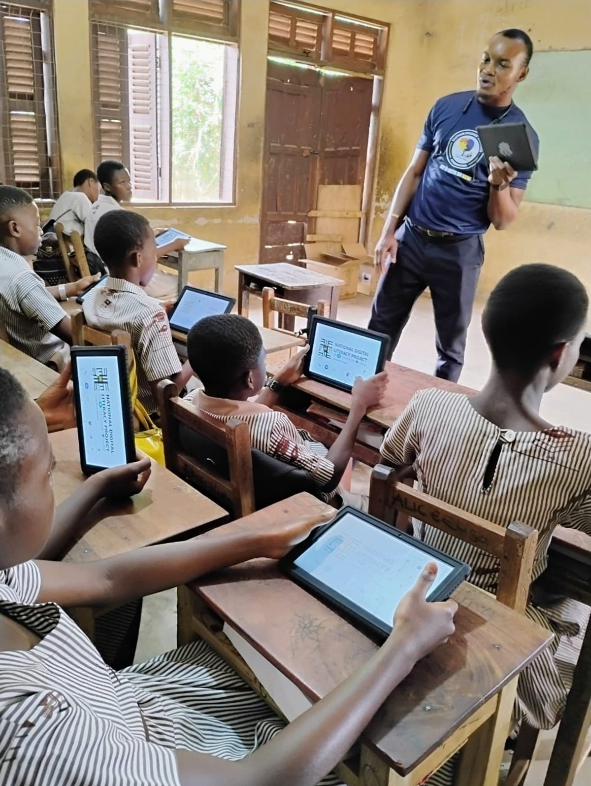 Teacher holding National Digital Literacy Project tablet in classroom, Wa
