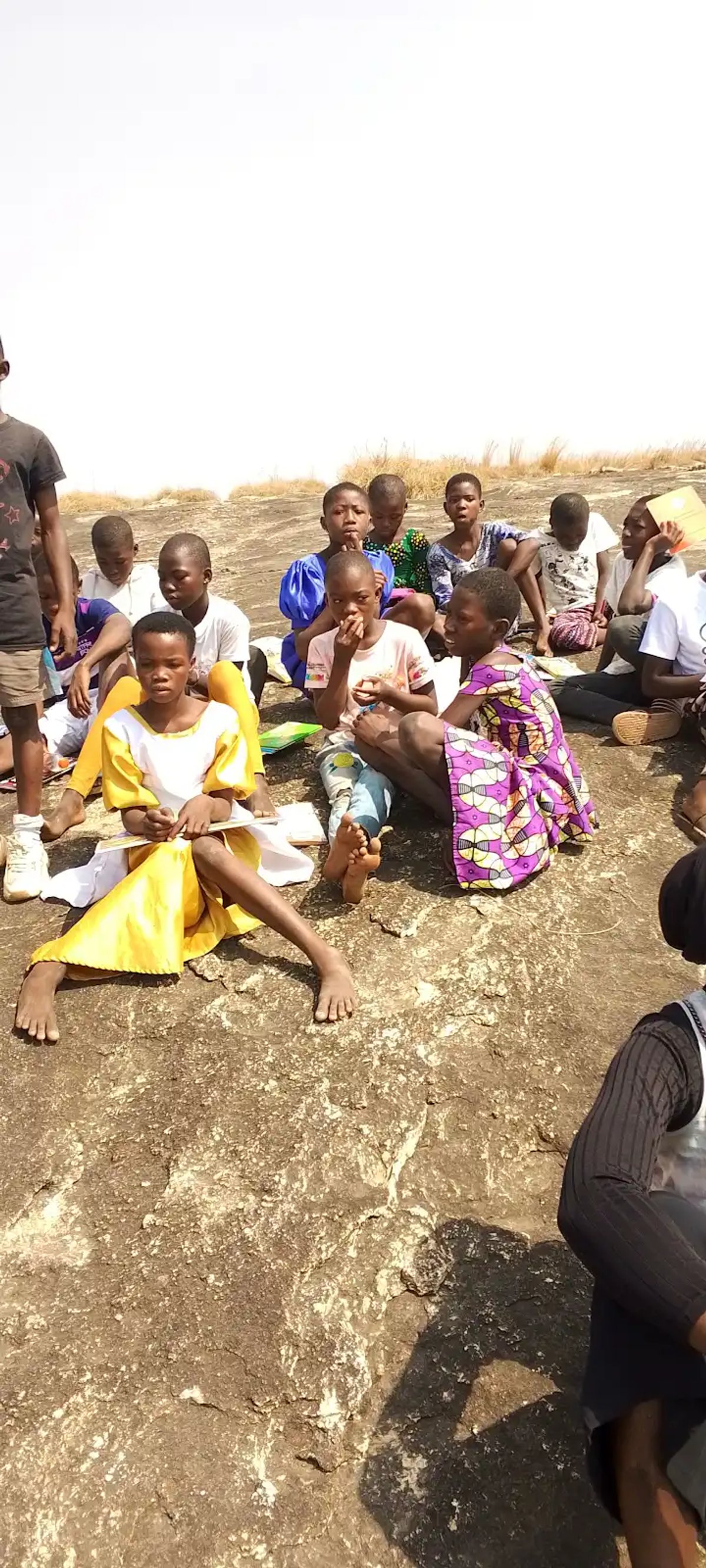 Children sitting on the surface of Uombo Rock with books, Upper West Region