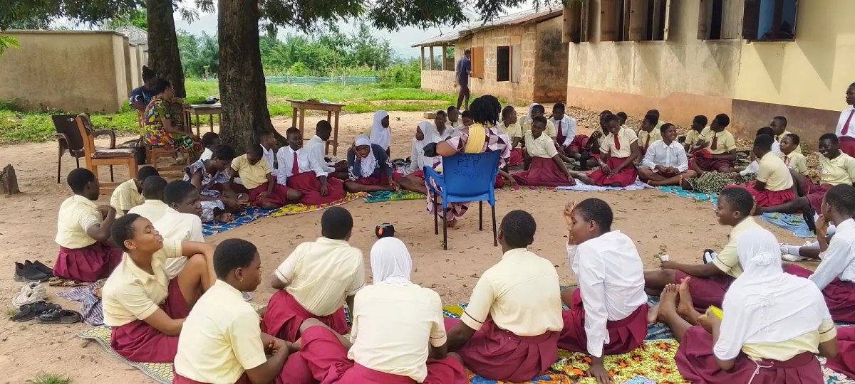 Large group of students in cream and burgundy uniforms sitting in a circle for a leadership session