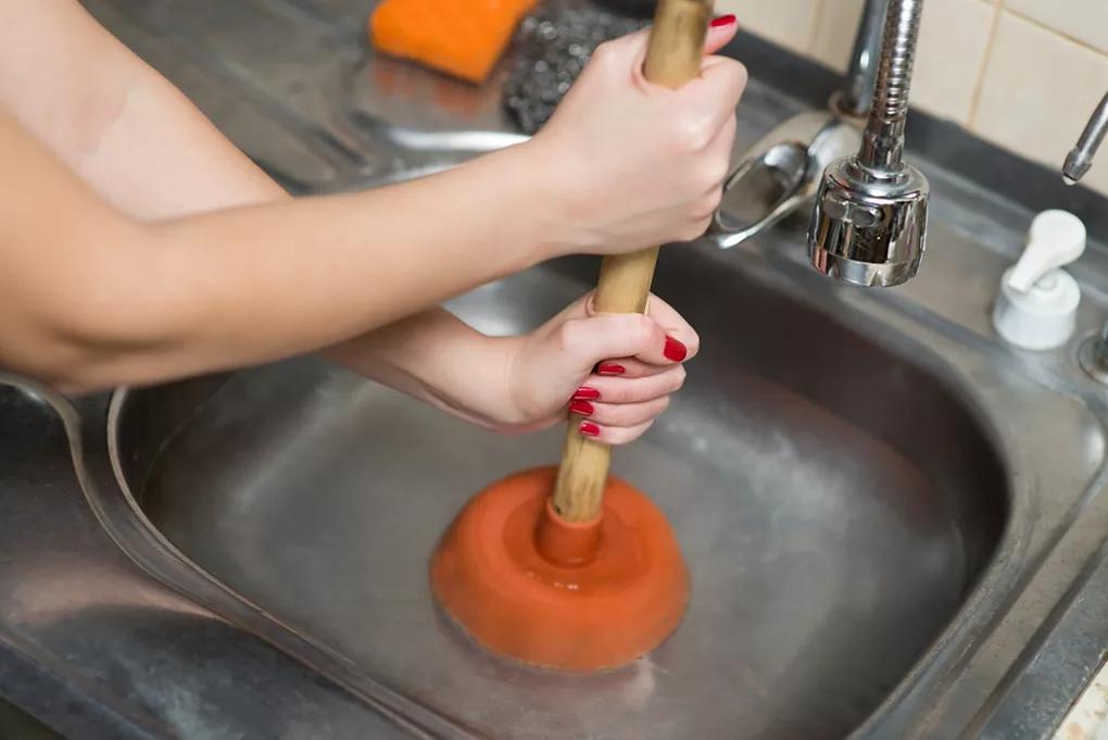 Using a plunger to unblock a sink, with water partially filling the sink.