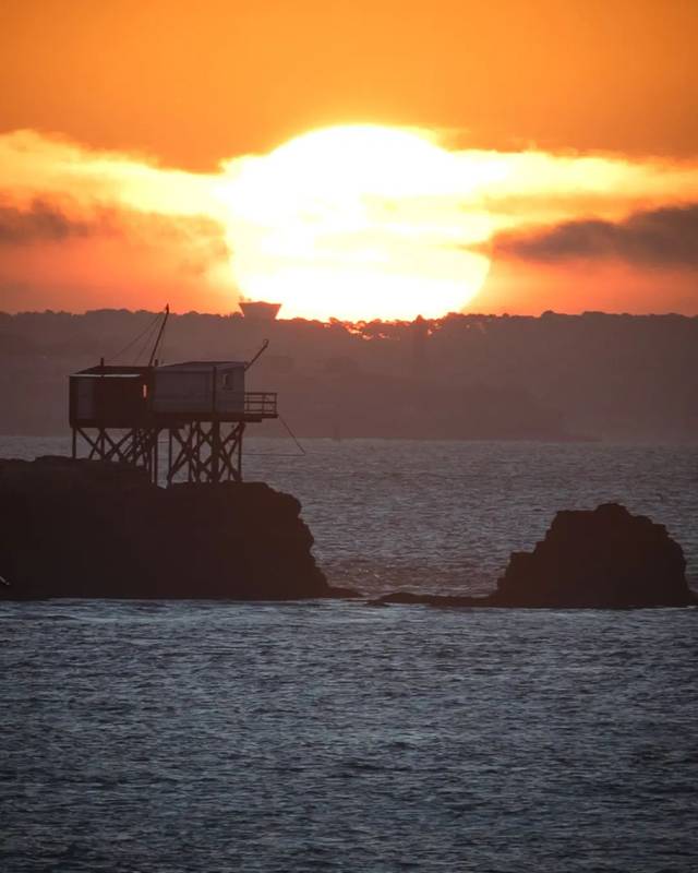 Grand soleil orange derrière un carrelet sur la côte