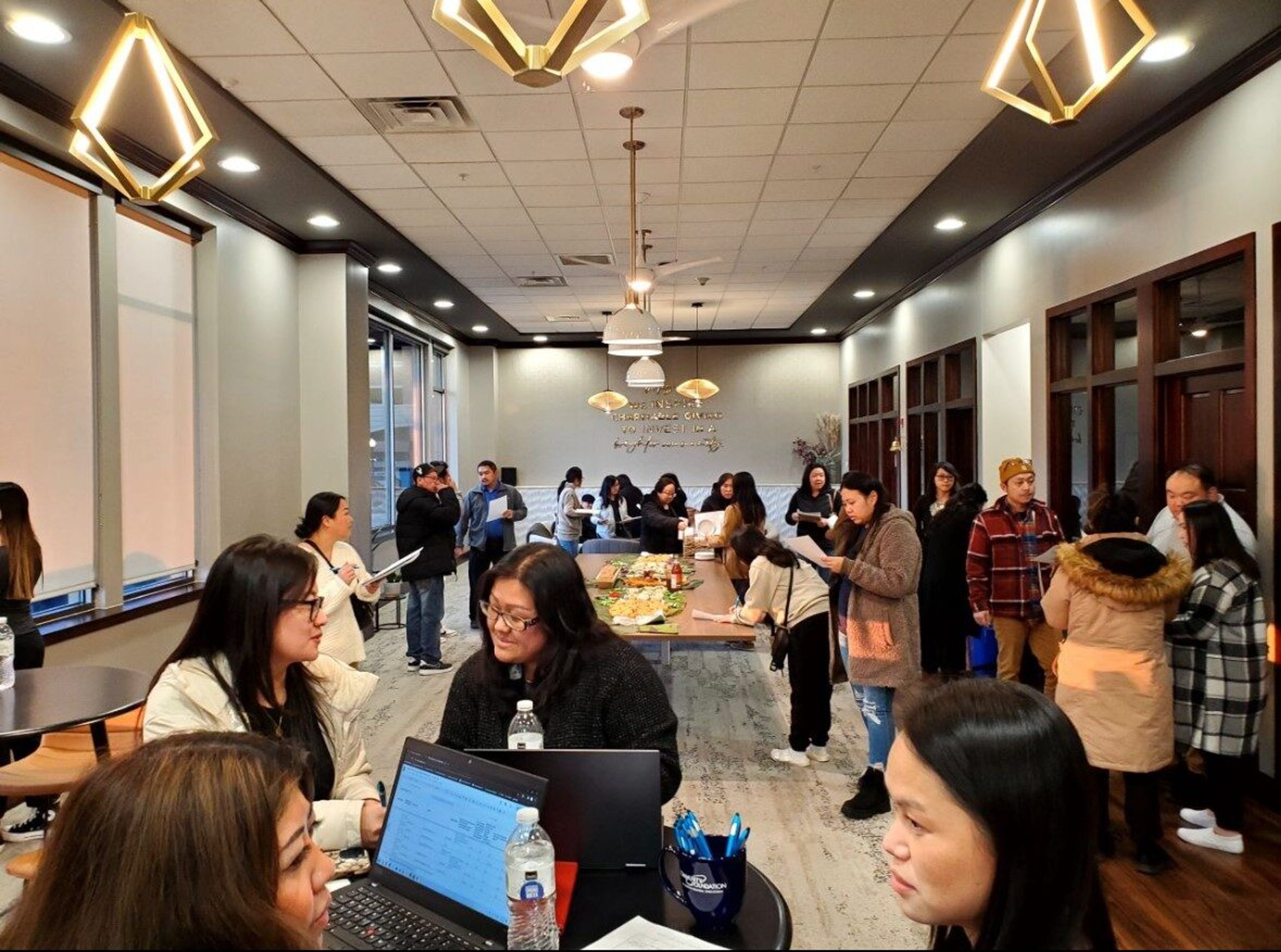 Neighbours filling a community connection centre, some working at laptops while others gather around a table of shared food.