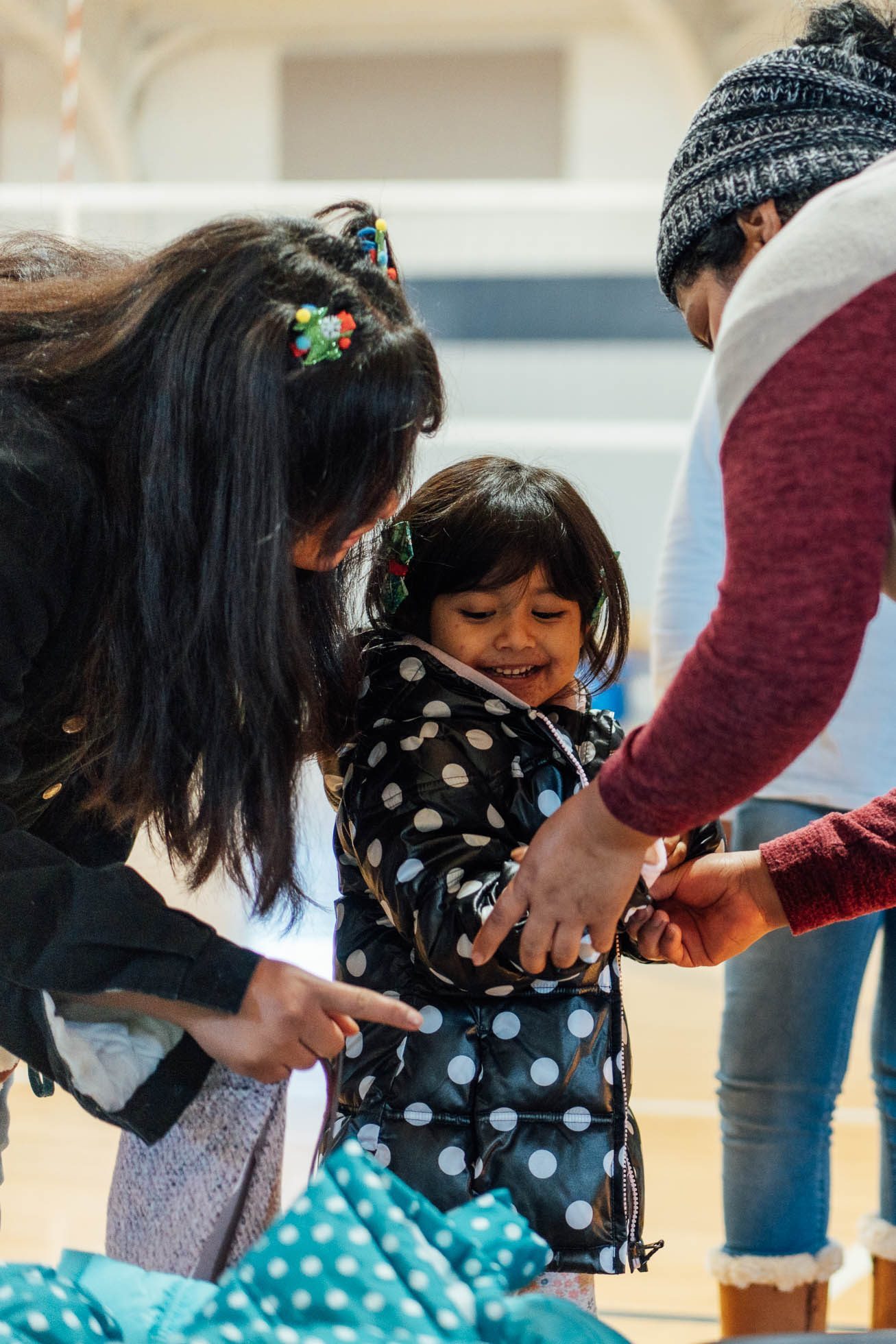 A volunteer helping a smiling young girl try on a new winter coat while another woman looks on, in Marshfield.