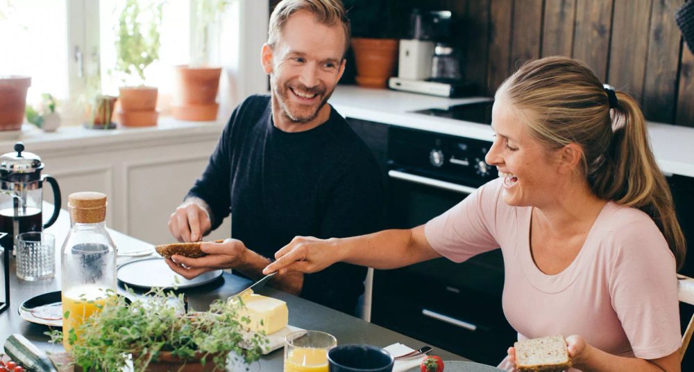 To personer ler rundt frokostbordet og smører brødskiver