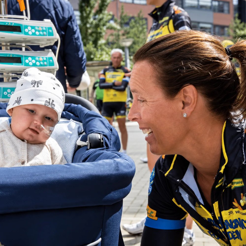 Syklist fra Team Rynkeby smiler til et lite barn i barnevogn utenfor sykehuset