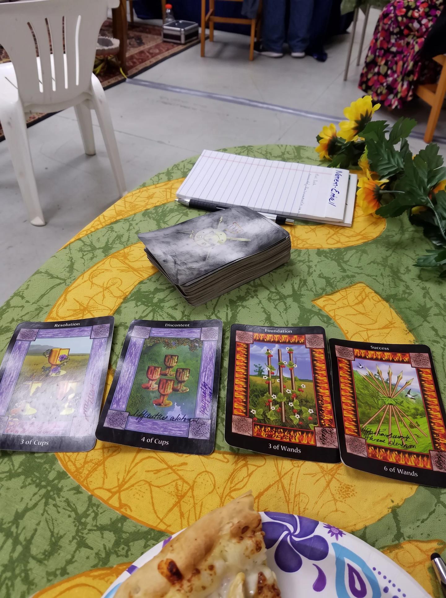 Four oracle cards spread across a green reading cloth beside sunflowers and a notebook