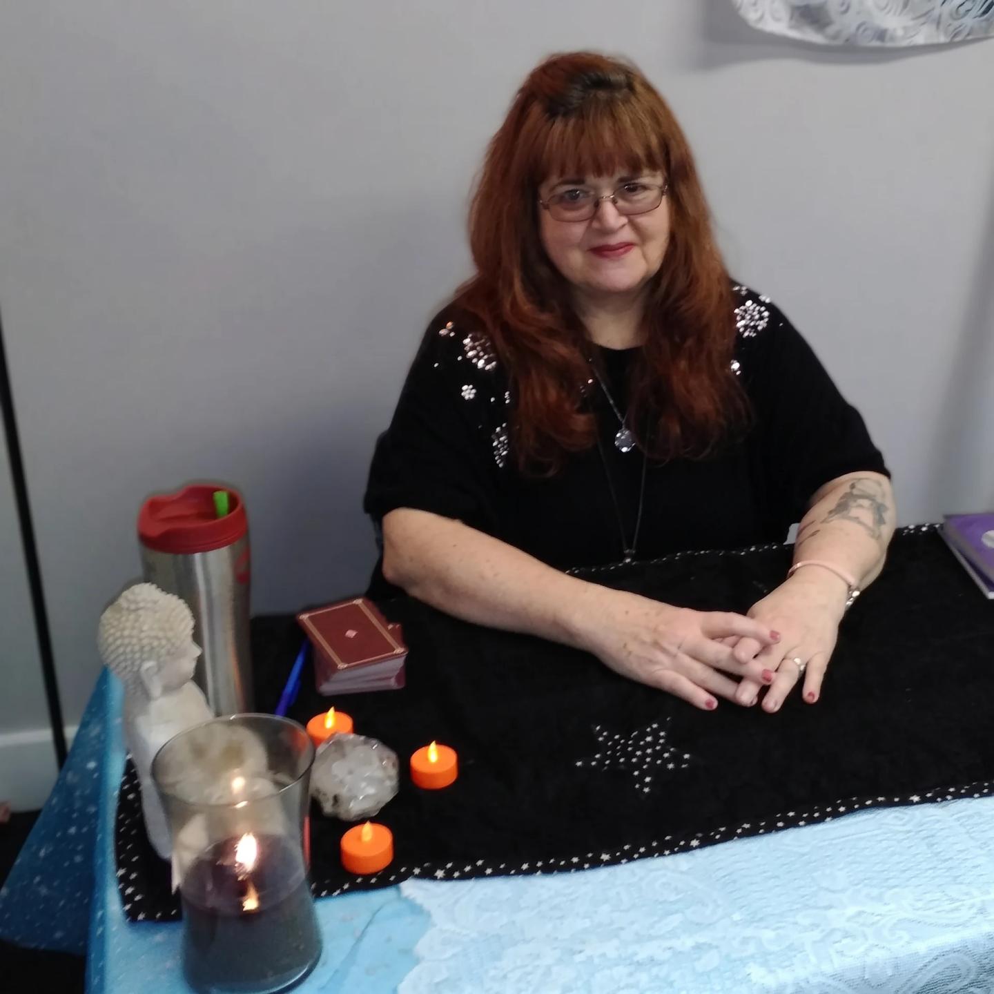 Rev. Berta Kay seated behind a candlelit psychic medium reading table