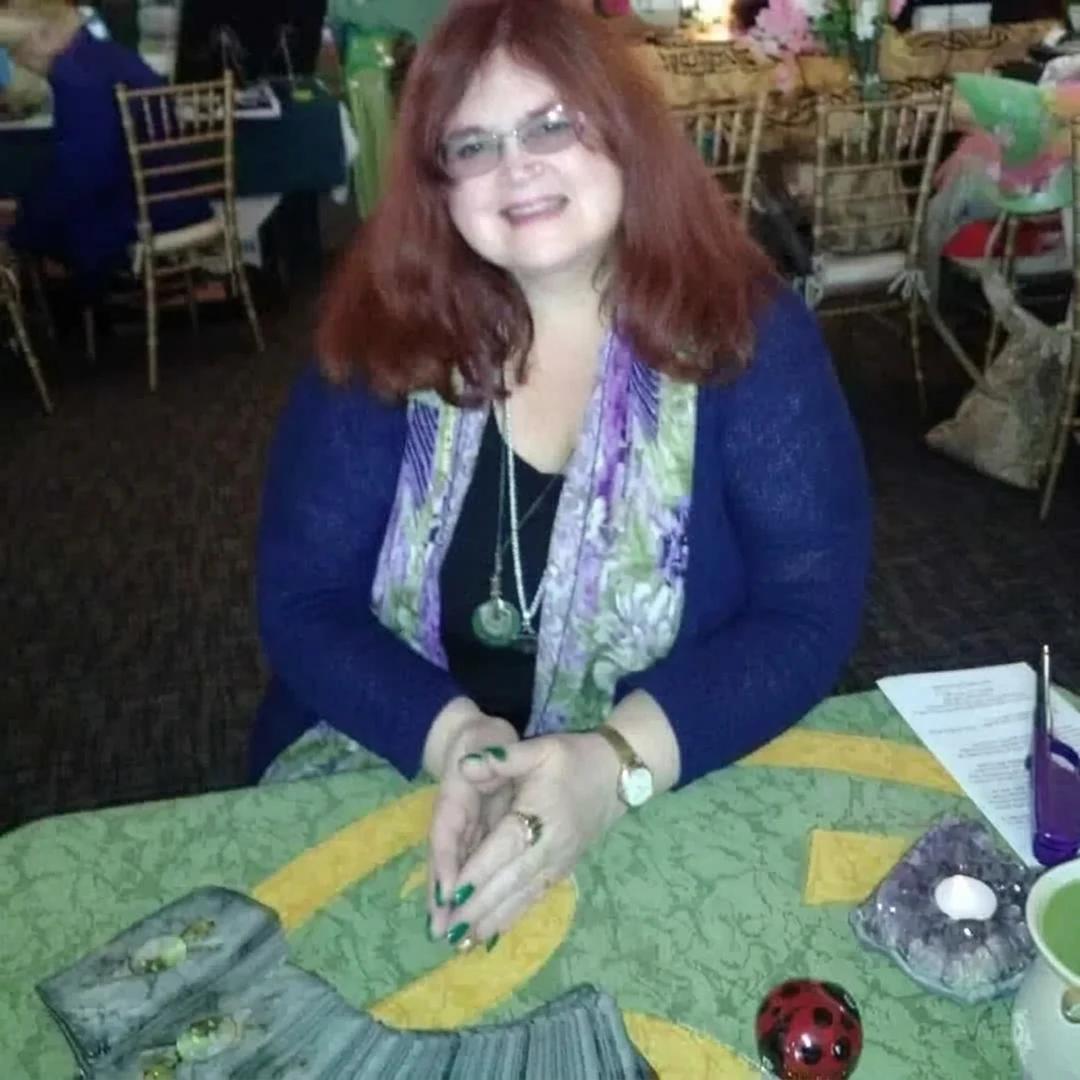 Rev. Berta Kay seated at her green reading table with tarot cards and a candle