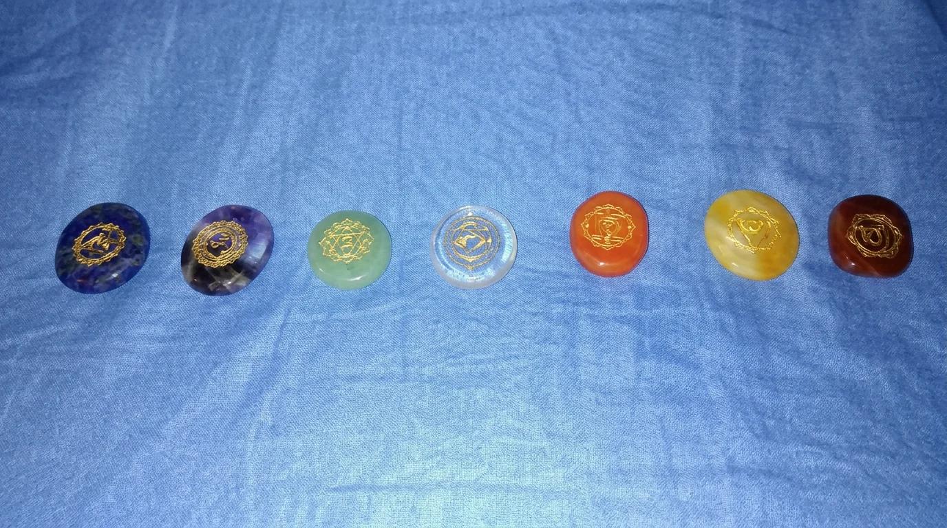 Seven polished chakra stones arranged in a row on blue cloth for Reiki healing
