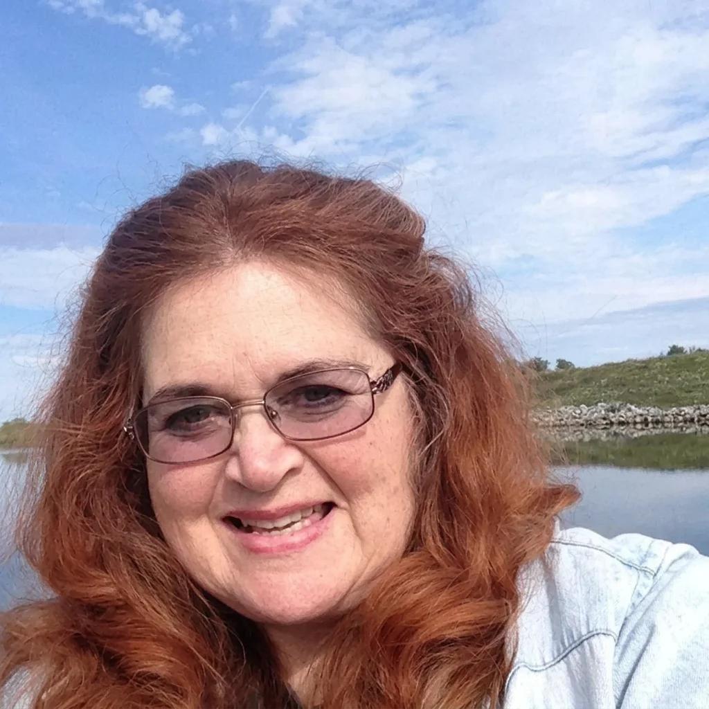 Rev. Berta Kay smiling outdoors beside calm water under a blue sky