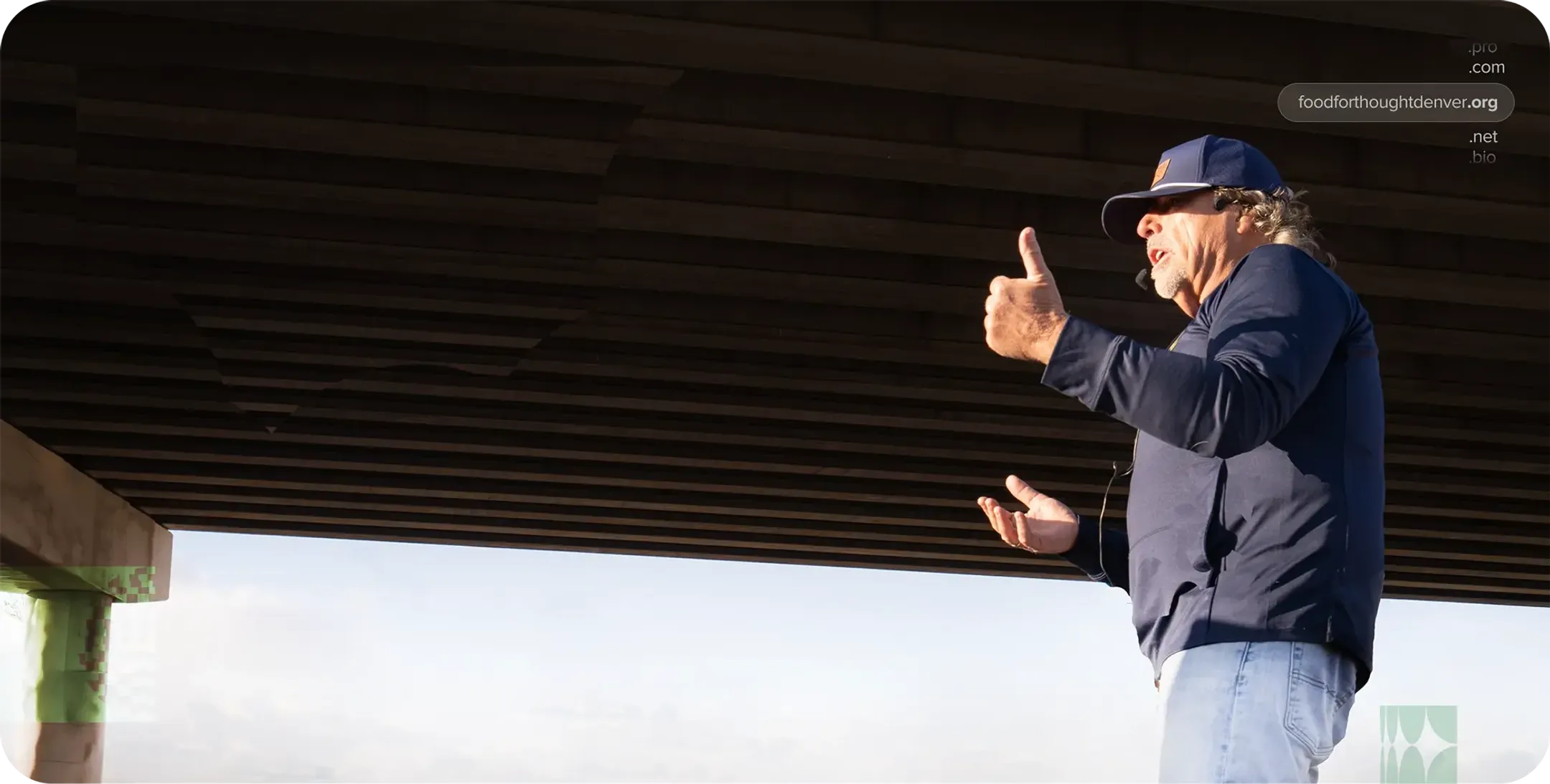 A man wearing a jacket and hat is giving a speech to a group of people off frame.