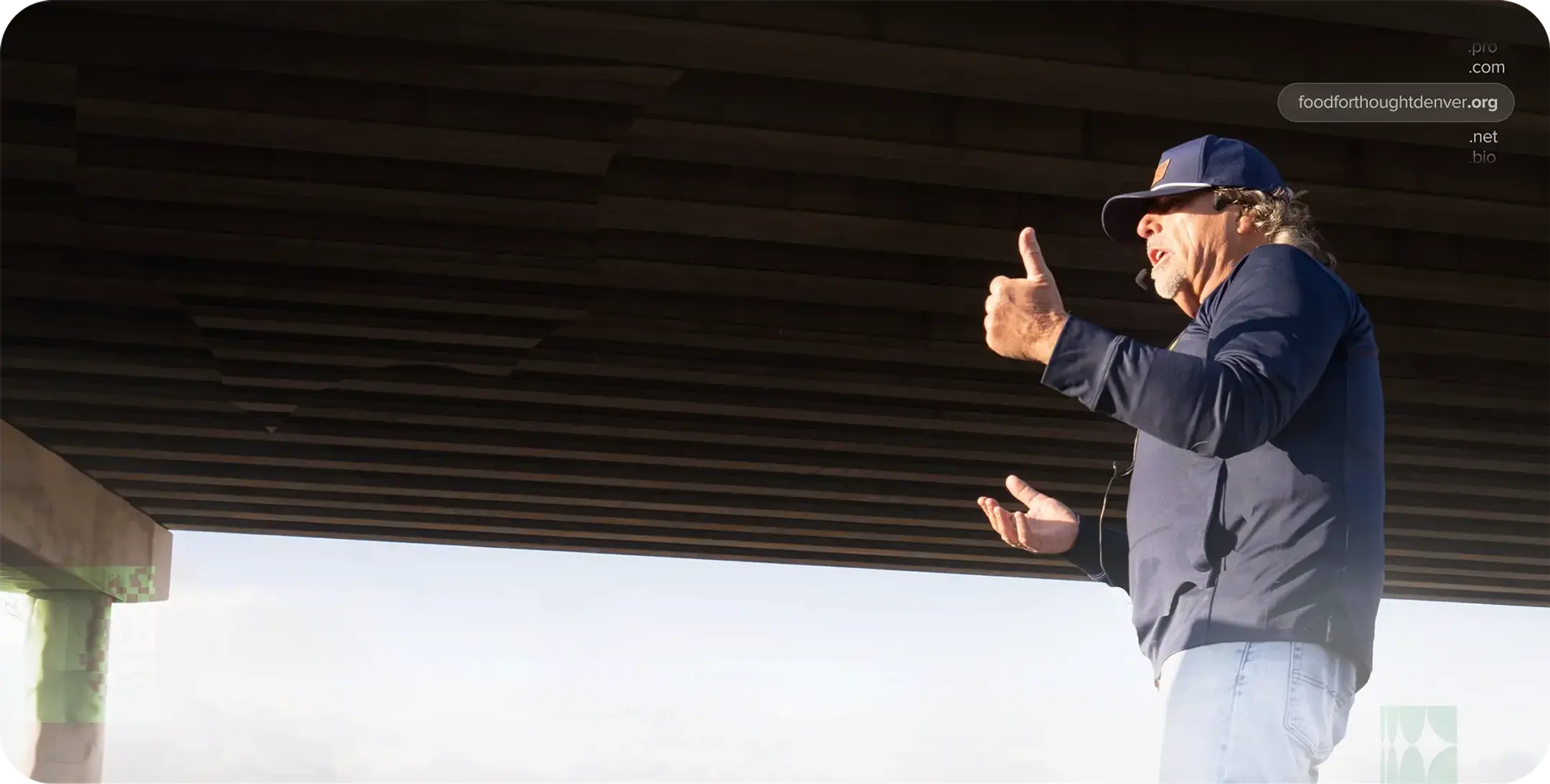A man wearing a jacket and hat is giving a speech to a group of people off frame.