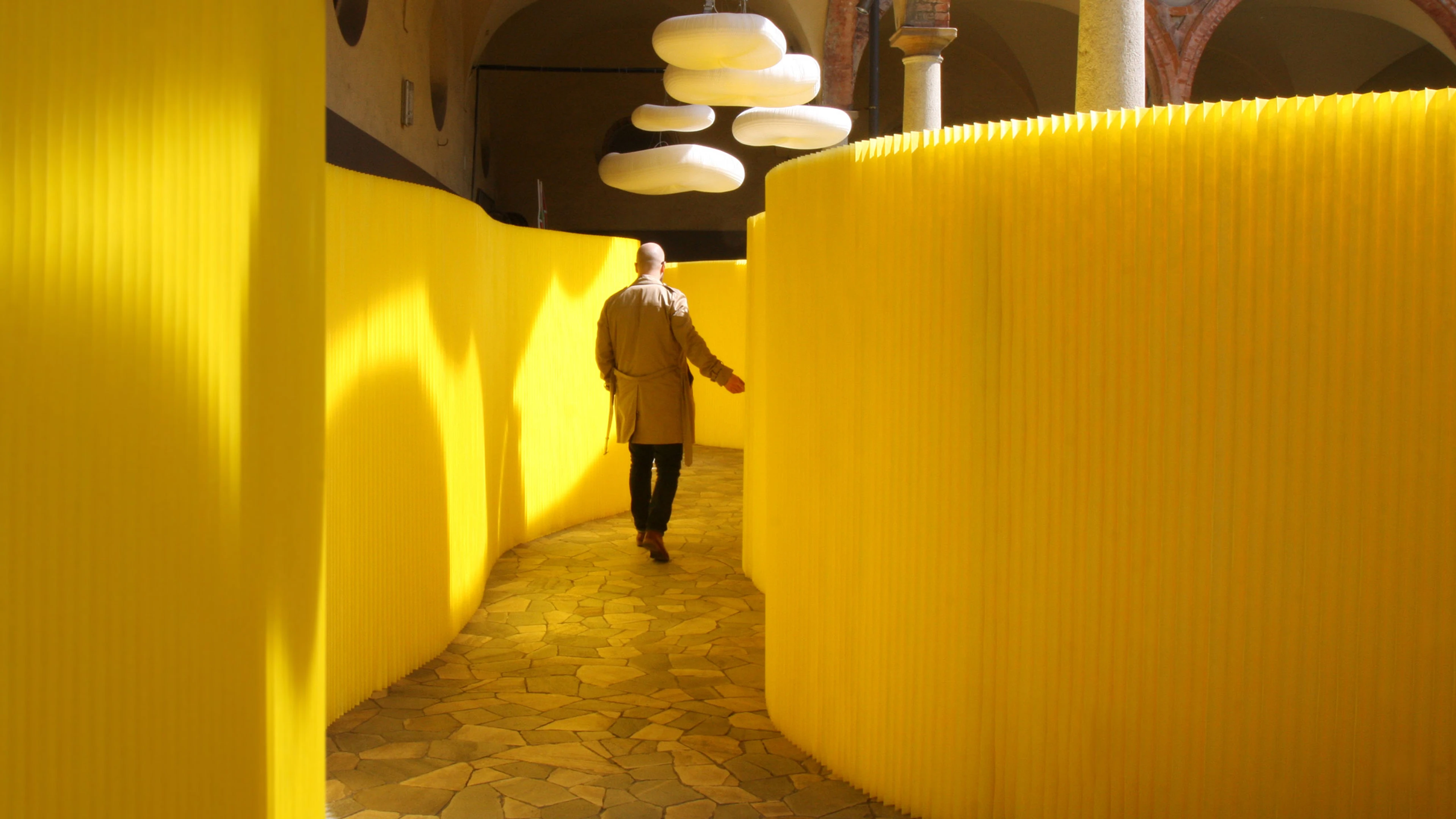 A man strolls along a hallway created from yellow textile softwalls at the paper music exhibit in Milan.