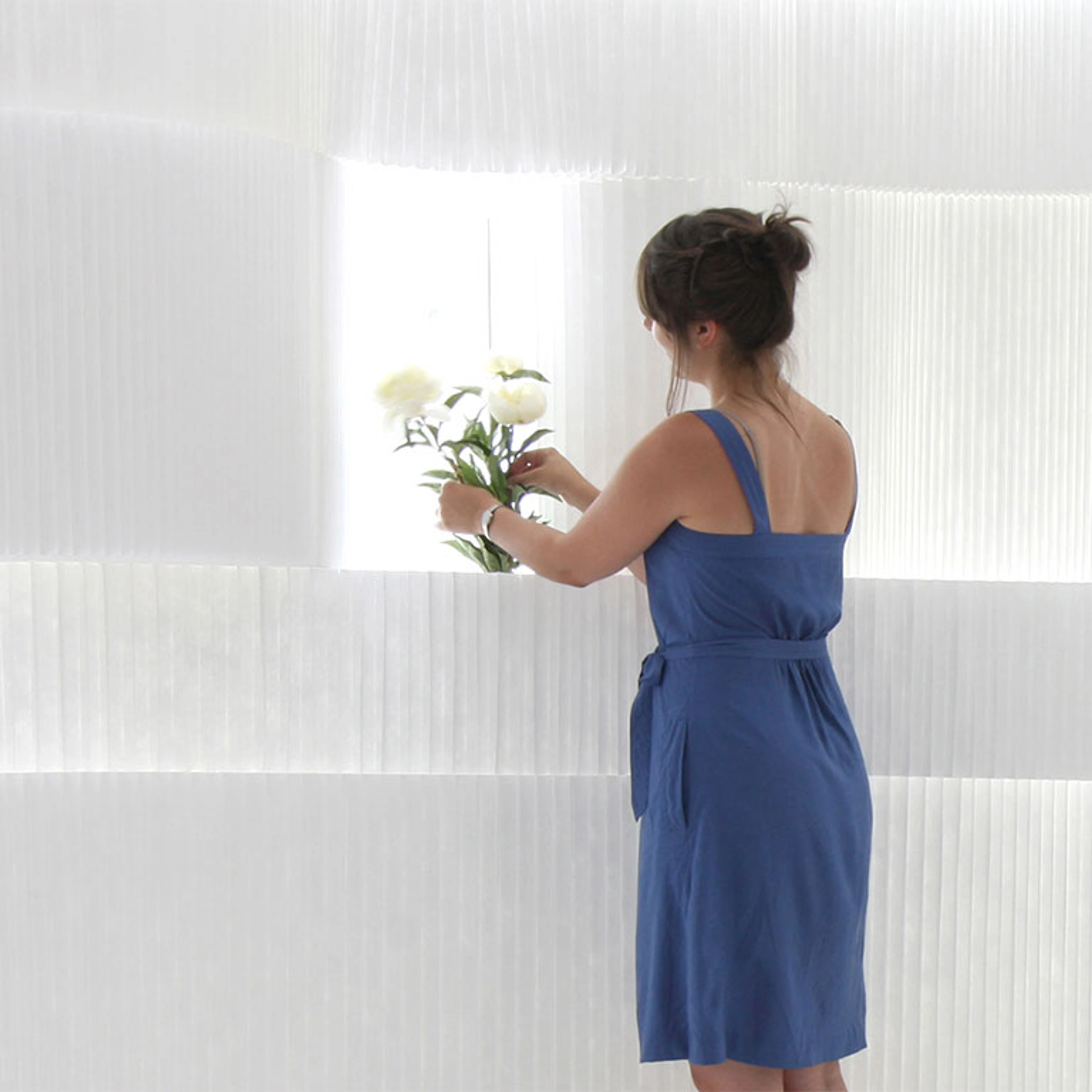 woman inserts a glass vase filled with a bouquet into a wall of white textile softblocks