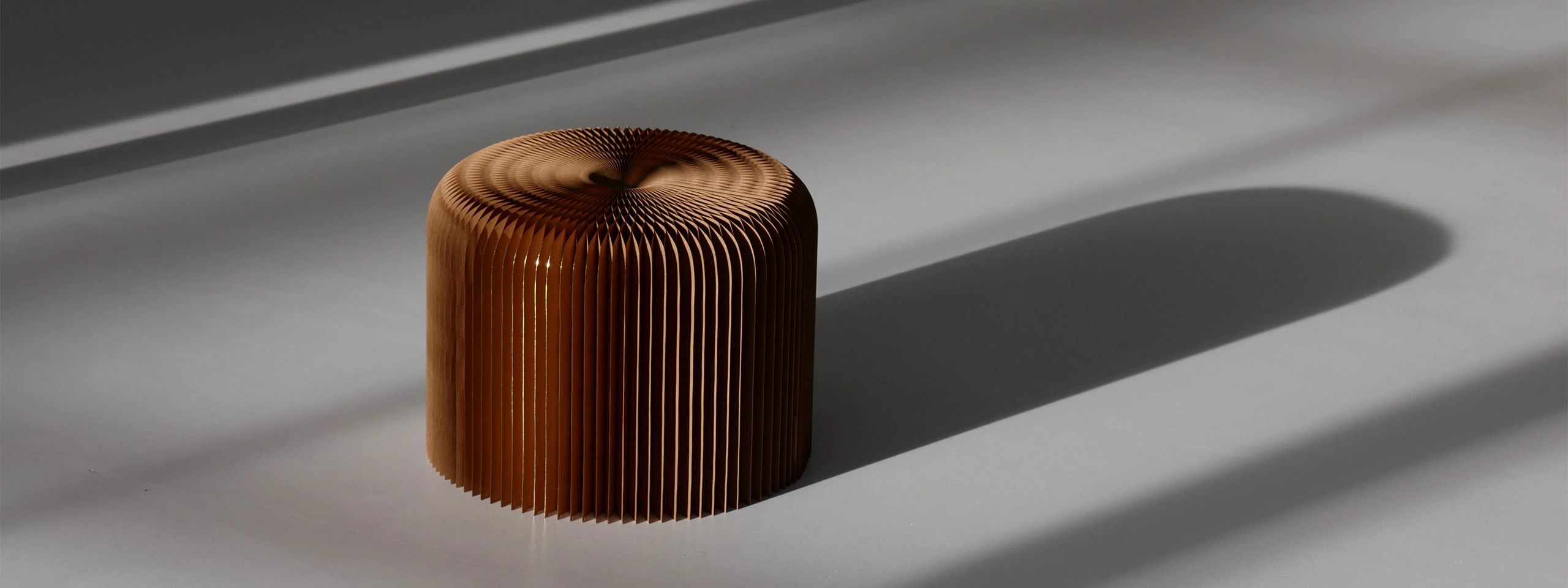 gilded paper softseating fanning stool casts a long shadow on the ground