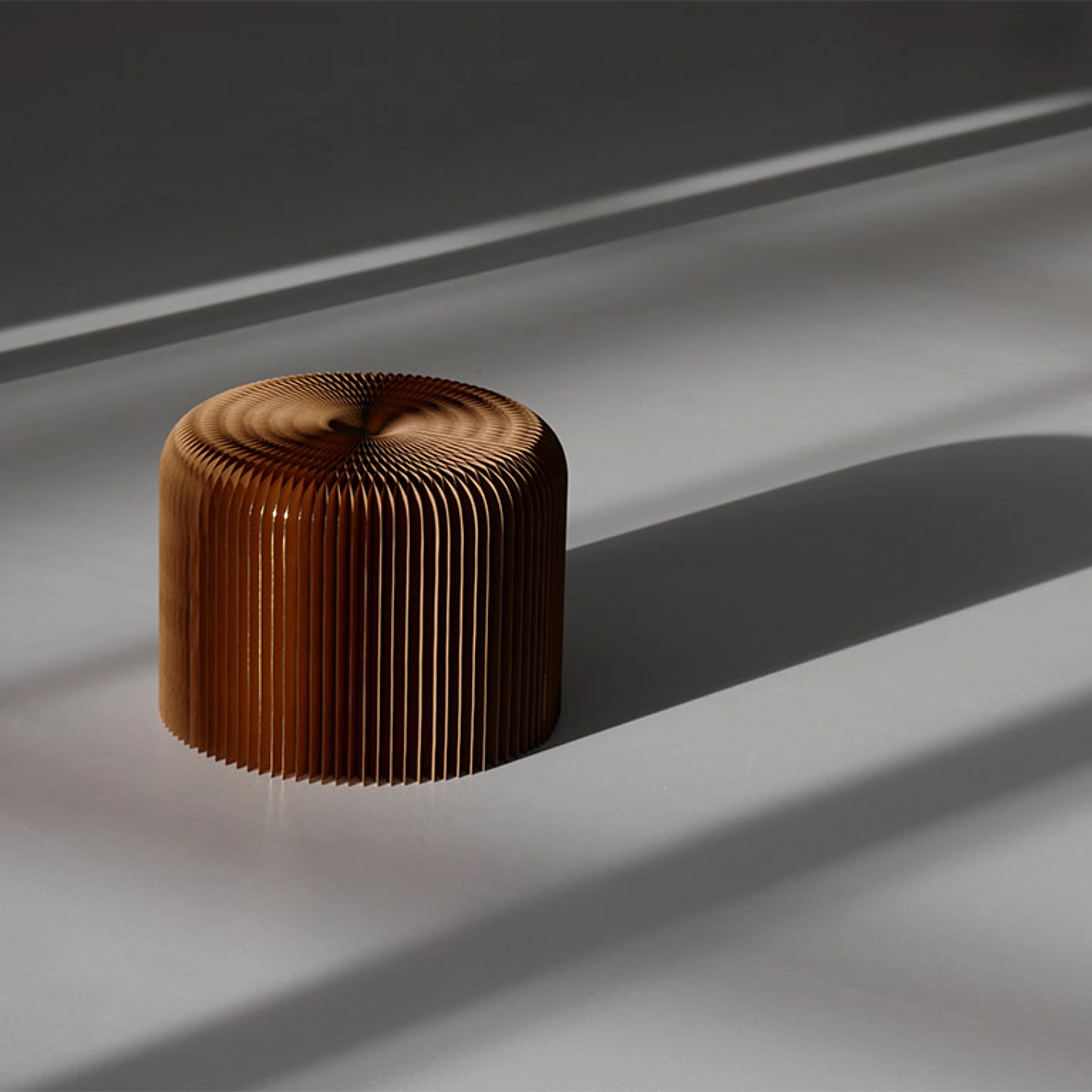 a gilded paper softseating fanning stool casts a long shadow on the ground