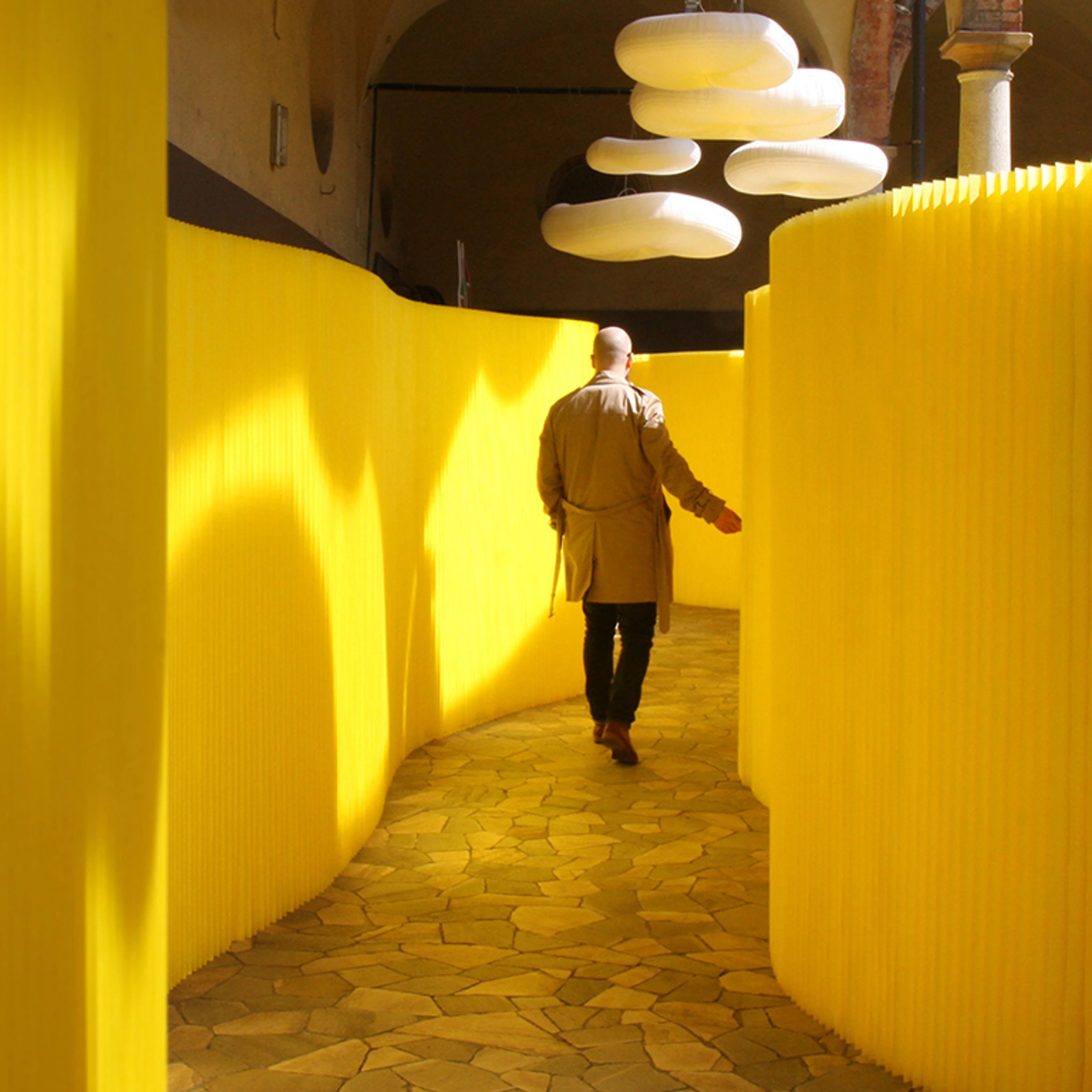 A man strolls through a hallway of yellow textile softwalls at the paper music exhibit in Milan.