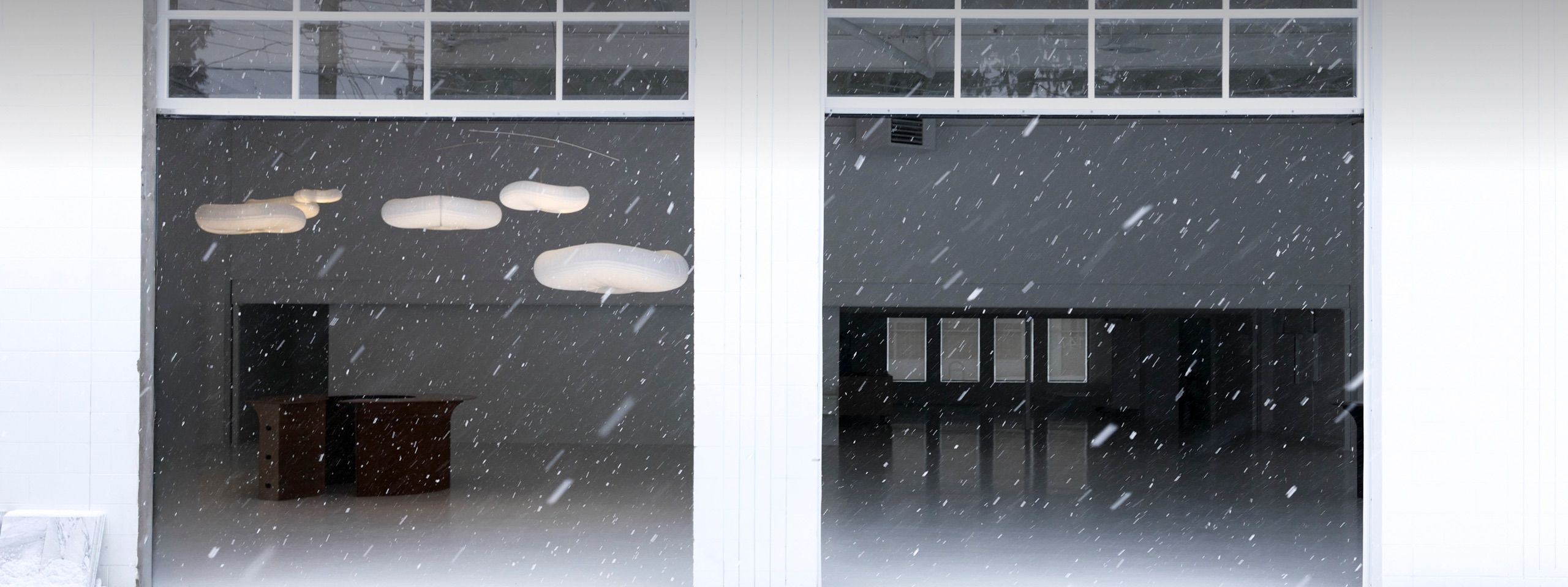 molo softlights suspended inside a minimalist industrial space, glowing warmly against falling snow and a white architectural backdrop.
