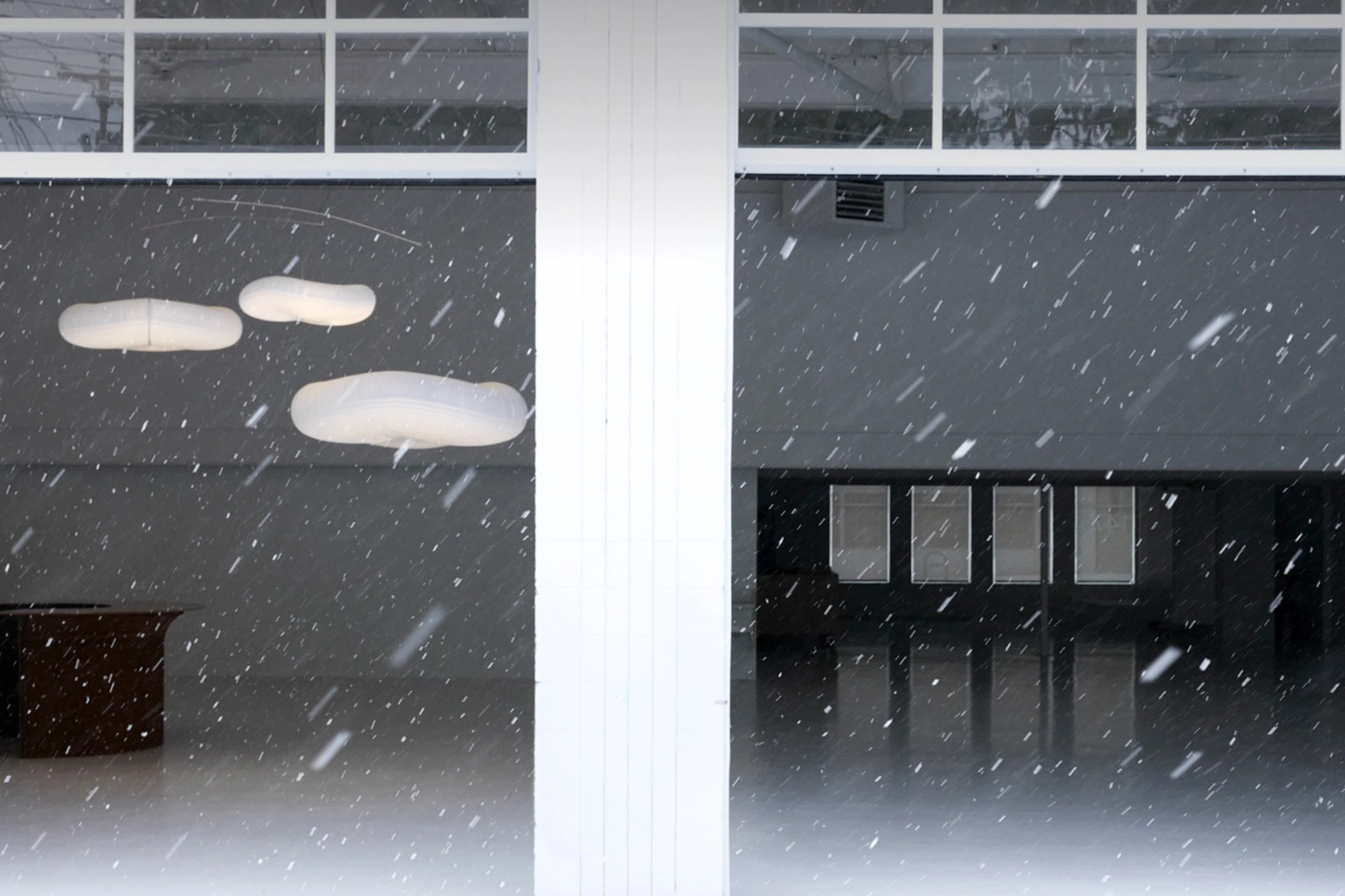 molo softlights suspended inside a minimalist industrial space, glowing warmly against falling snow and a white architectural backdrop.
